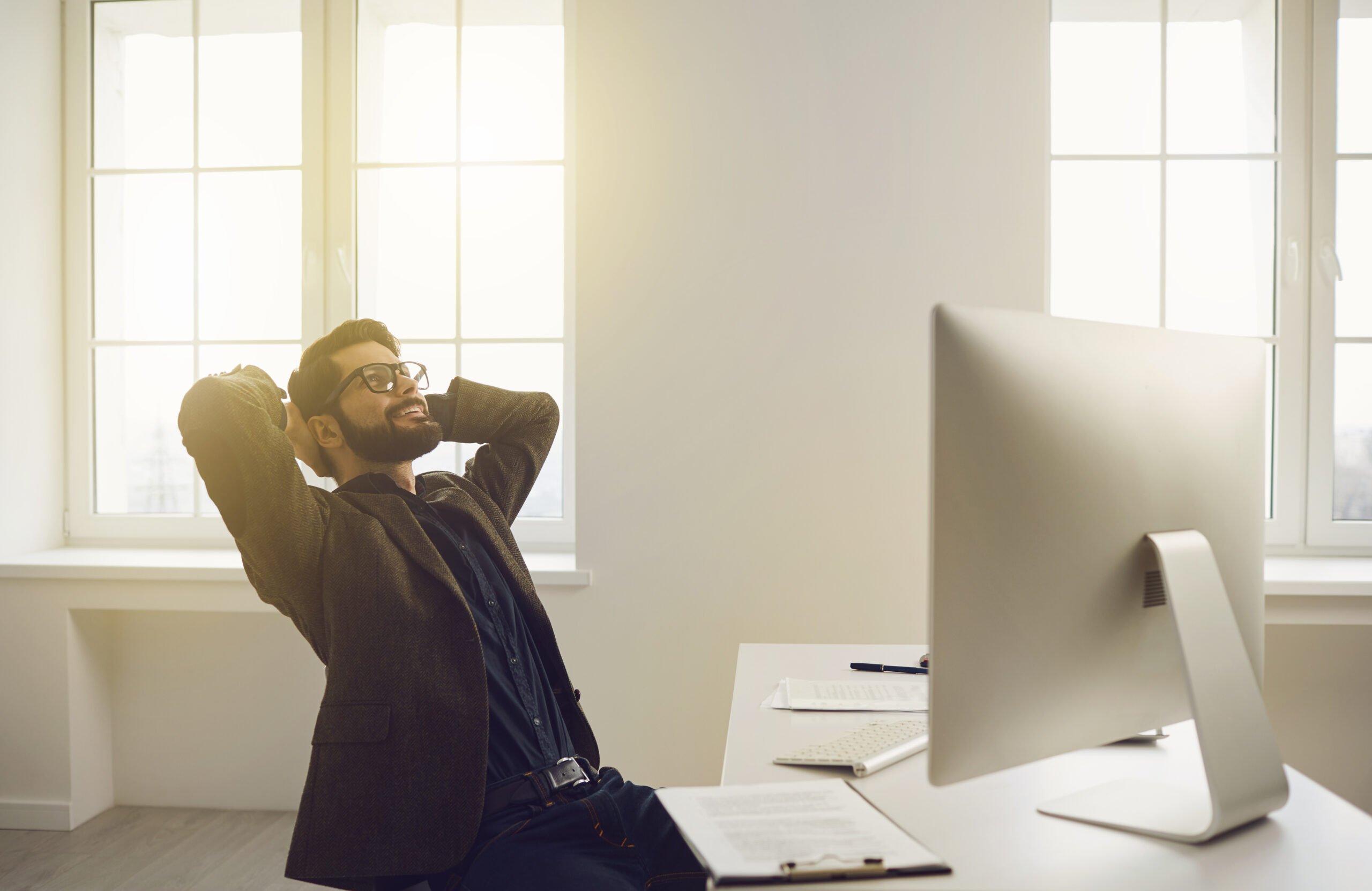 Businessman in glasses hands behind head contented dreams happy smiling sitting at a table in the office. Successful working day at work.