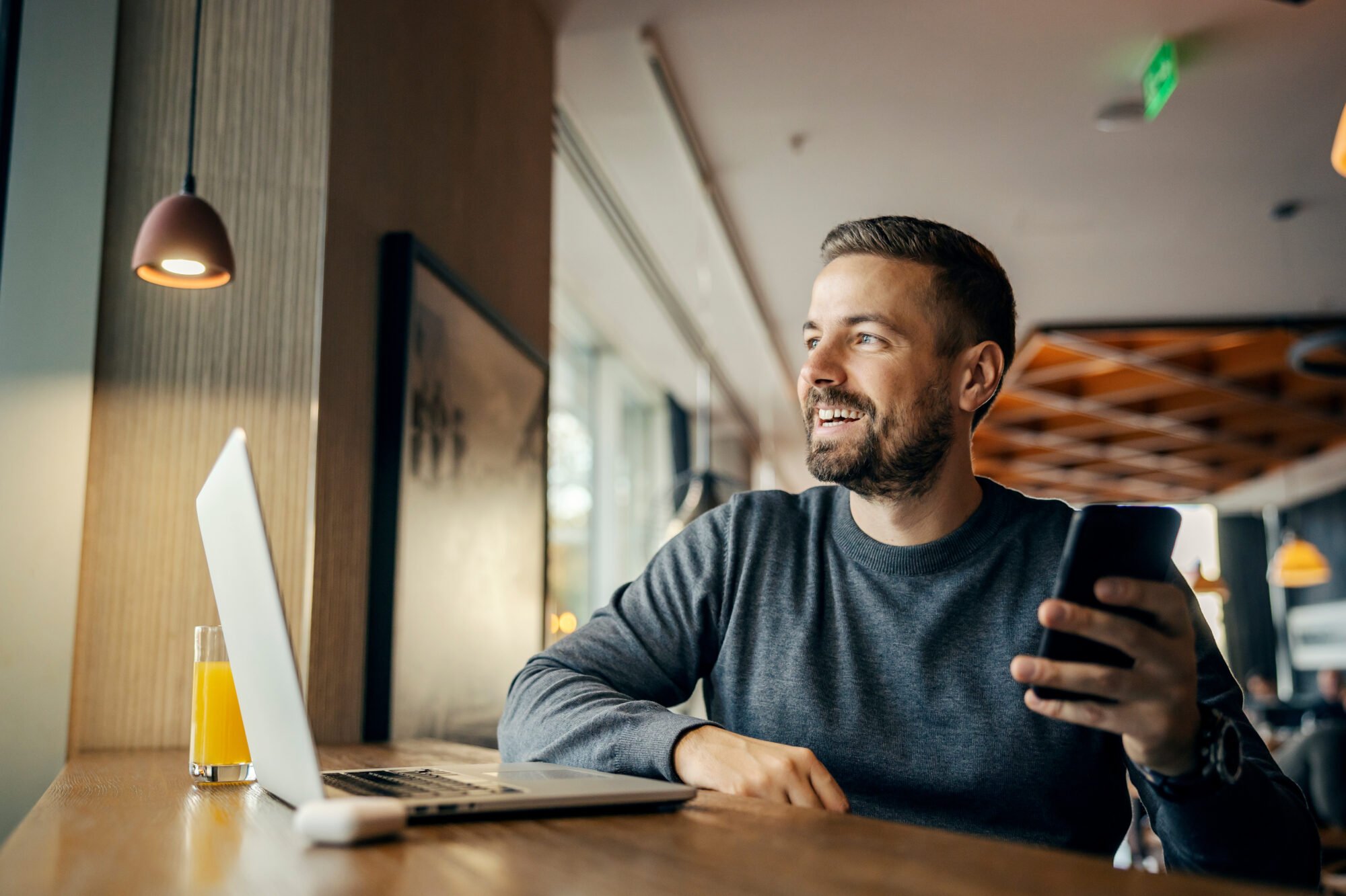 A happy freelancer is working on social media by using multiple technologies at coffee shop.