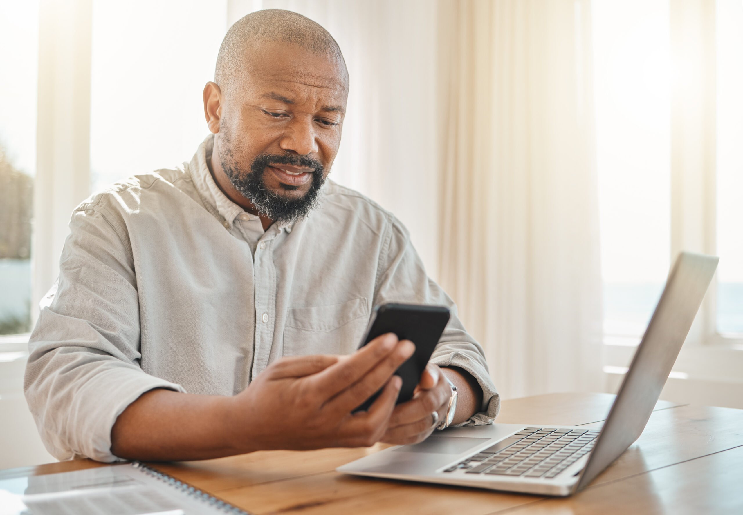 Phone, laptop and remote work with a black man checking his debt or banking from the home office. Pension, contact and communication with senior male working on finance in a living room of his house.